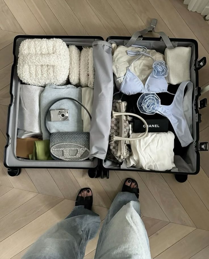 ♱ Open suitcase with neatly packed clothes, bags, and shoes on a wooden floor. | Sky Rye Design Open suitcase with neatly packed clothes, bags, and shoes on a wooden floor.