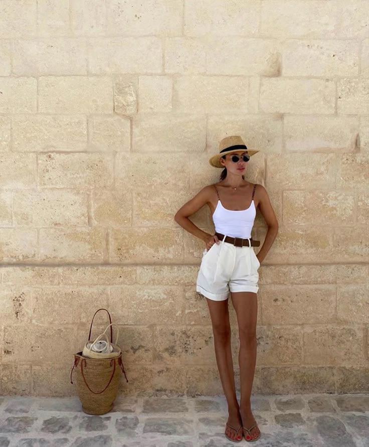 🦋 Stylish woman in summer outfit with hat, leaning against a stone wall with a straw bag nearby. | Sky Rye Design Stylish woman in summer outfit with hat, leaning against a stone wall with a straw bag nearby.