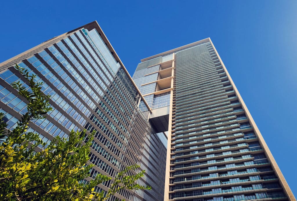 Modern skyscrapers and greenery under clear blue sky, showcasing urban architecture.