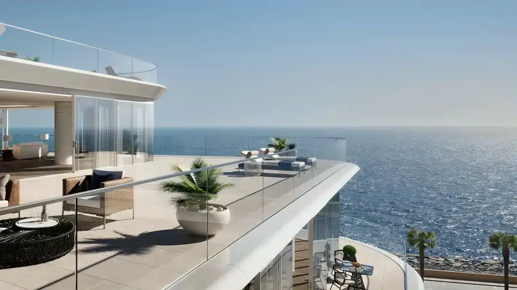Modern oceanfront terrace with glass railings and luxury furniture overlooking a serene blue sea.