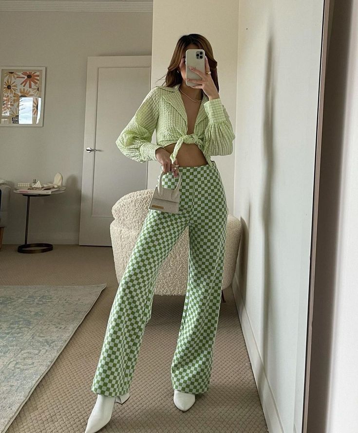 Fashionable outfit with green checkered pants, crop top, white boots, and mini bag in modern room setting.