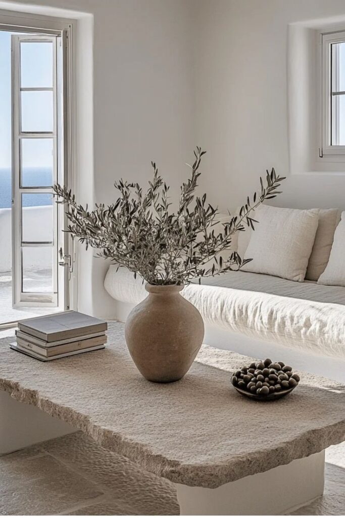 Cozy minimalist living room with stone table, vase, and sea view through an open window.
