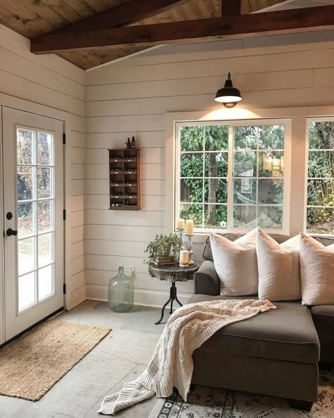 Cozy living room with sectional sofa, pillows, and natural light through large windows, featuring rustic decor elements.