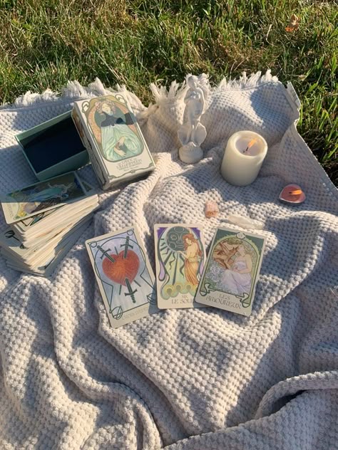 127481cae8d7a848db7389cba9fc0f70 Tarot cards on a blanket with a candle and angel figurine, set outdoors on grass during a sunny day. | Sky Rye Design Tarot cards on a blanket with a candle and angel figurine, set outdoors on grass during a sunny day.