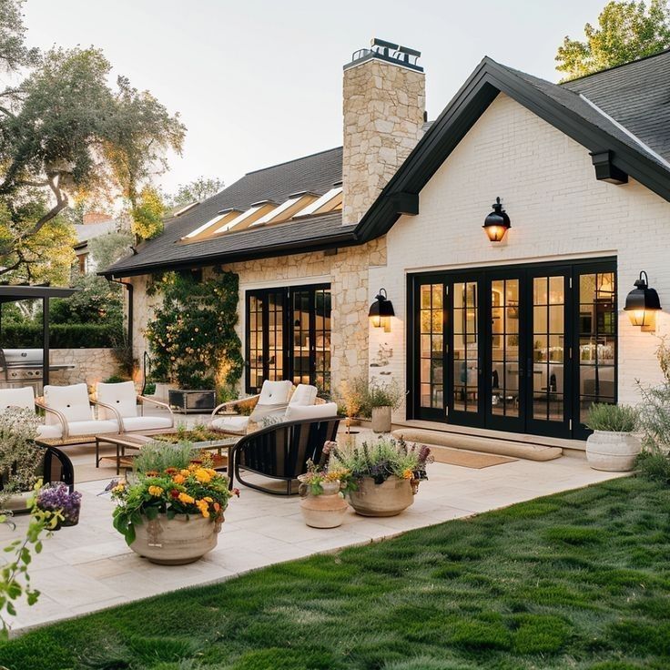 Elegant patio with cozy seating, lush greenery, and a charming stone house exterior under a clear sky. Perfect retreat.
