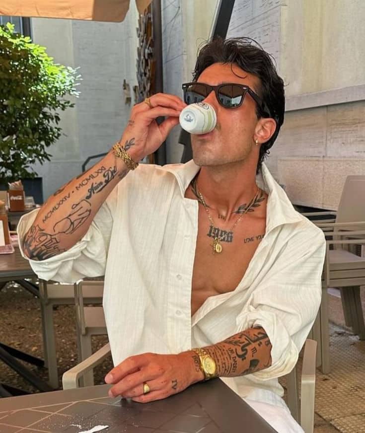 15 Bicep Tattoos For Women Man with sunglasses and tattoos enjoys an espresso in an outdoor cafe, wearing a white shirt. | Sky Rye Design Man with sunglasses and tattoos enjoys an espresso in an outdoor cafe, wearing a white shirt.