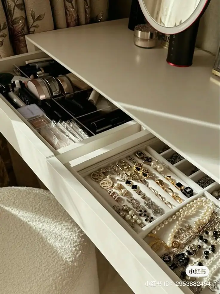 Vanity table with open drawers displaying organized jewelry and makeup under soft lighting.