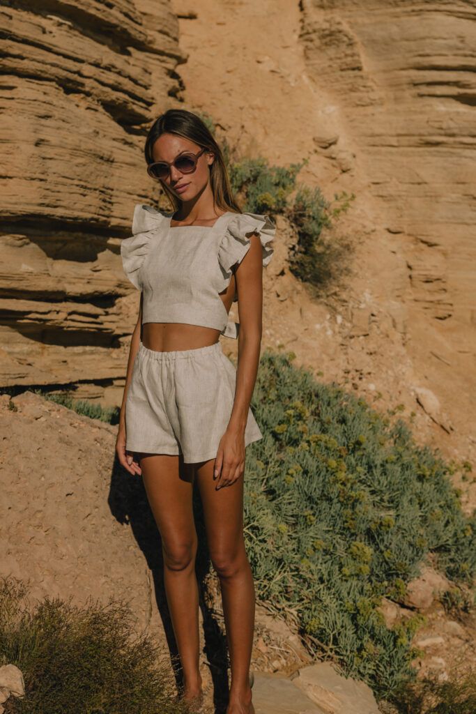 Woman in beige summer outfit and sunglasses poses by rocky desert landscape.