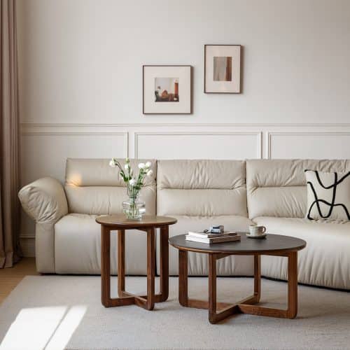 Modern living room with beige sofa, wooden coffee tables, and framed art on the wall. Minimalist decor and soft lighting.