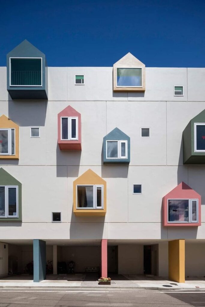 Colorful modern building with uniquely shaped windows against clear blue sky. Architectural design concept.