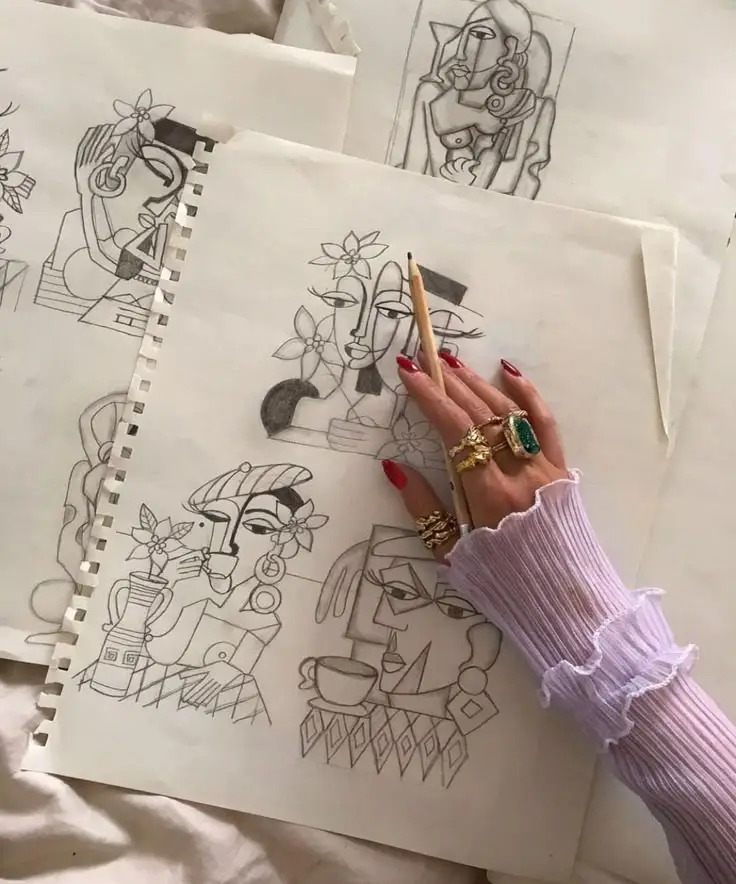 Hand drawing abstract sketches with pencil, adorned with rings, on a stack of art papers.