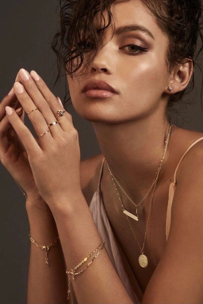 Woman with layered gold jewelry, featuring necklaces, rings, and bracelets, enhancing a sophisticated look.