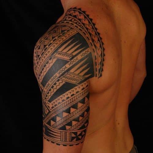 Tribal shoulder tattoo on a muscular arm with intricate geometric patterns, featuring bold black lines and shapes.