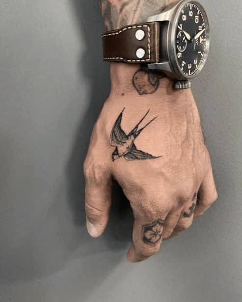 Hand with a swallow tattoo and a brown leather watch, showcasing artistic ink and classic timepiece style.