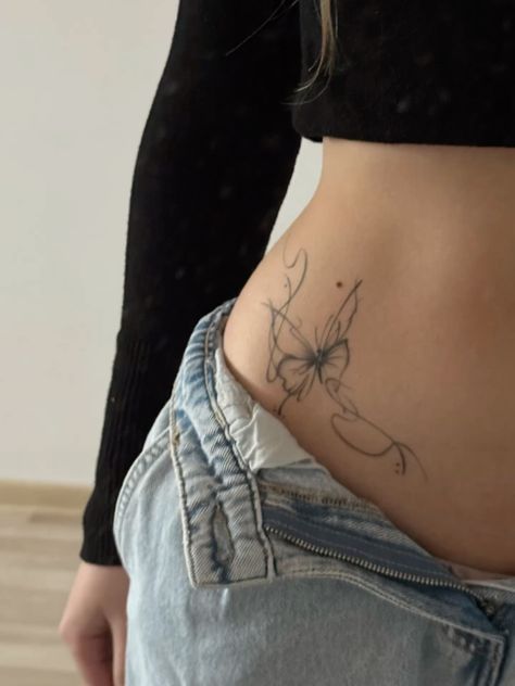 Butterfly tattoo on hip of person in jeans and black top, showcasing delicate design and stylish placement.