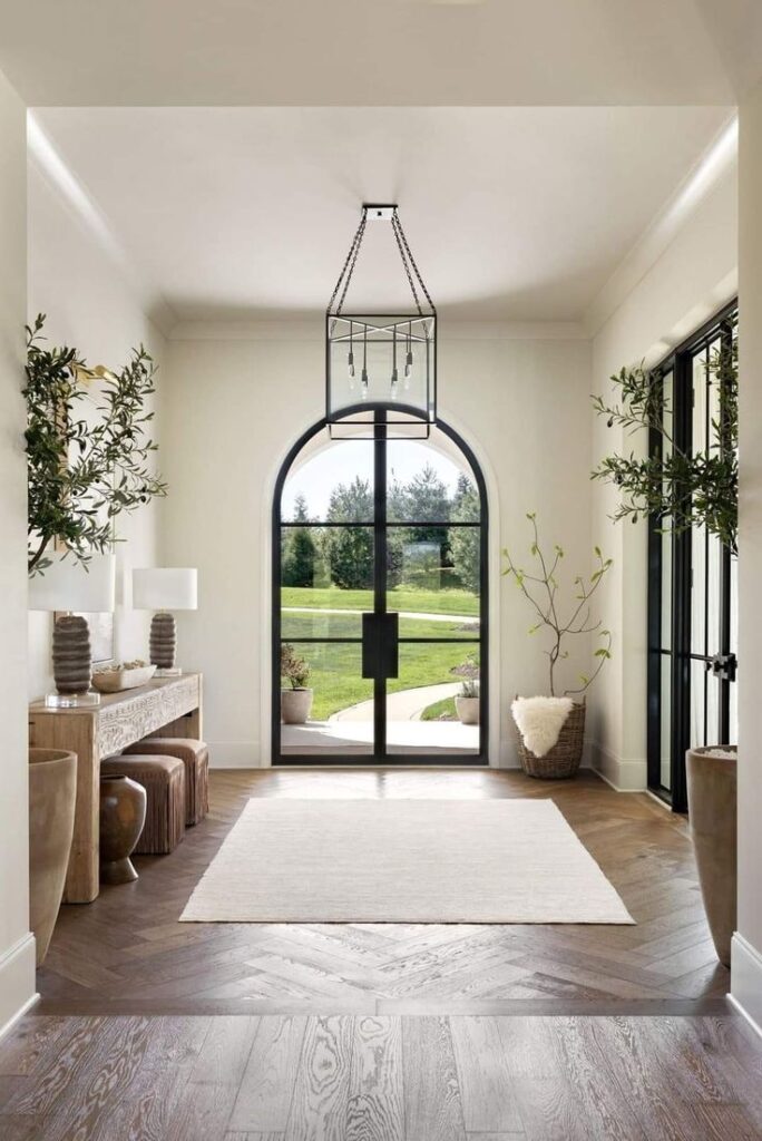 Elegant modern foyer with large arched window, wooden floor, and stylish decor.