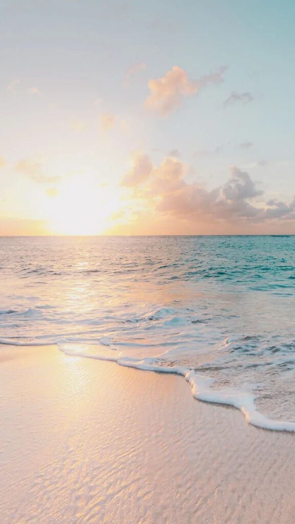 Serene beach sunset with gentle waves and soft pastel skies reflecting on the sandy shore.