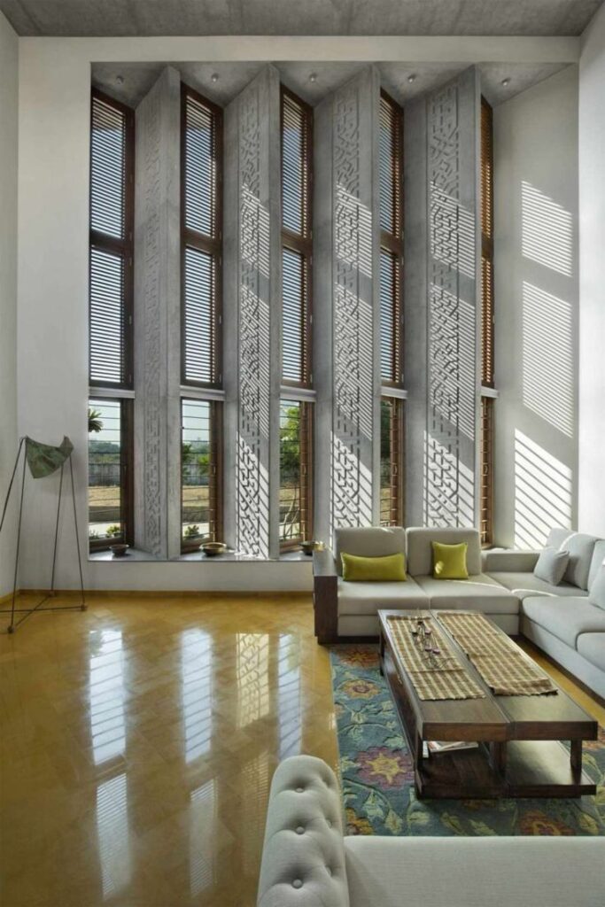Modern living room with tall windows, decorative panels, and cozy seating, showcasing natural light and elegant design.