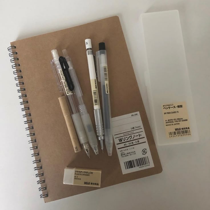 Muji stationery set with a brown spiral notebook, pens, eraser, and plastic pen case arranged neatly.