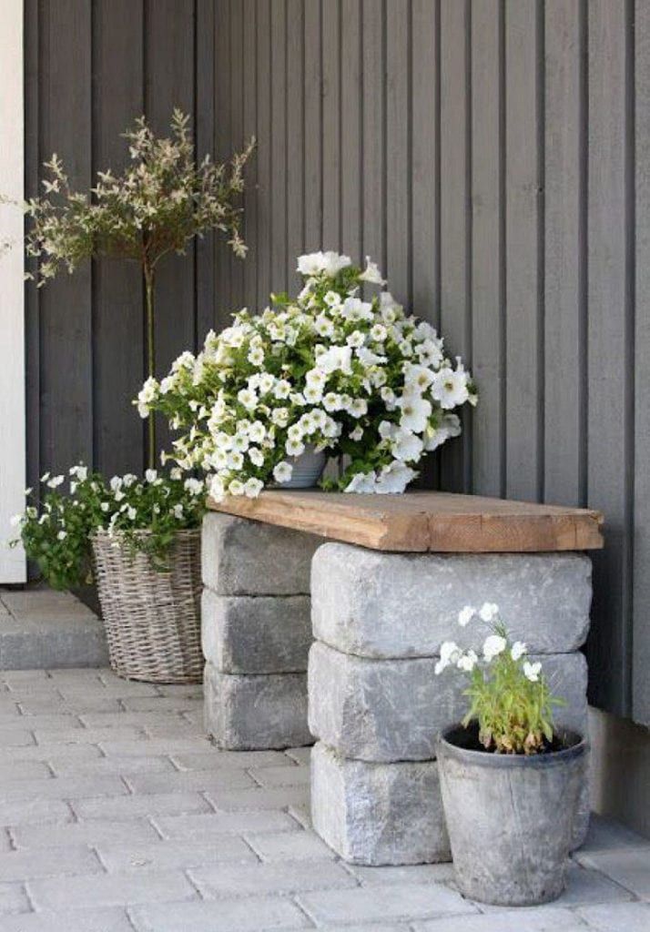 Rustic outdoor bench with flowers on stone pavers, perfect for a cozy garden corner.