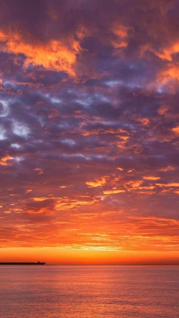 Vibrant orange and purple sunset over calm ocean waters and a distant horizon.