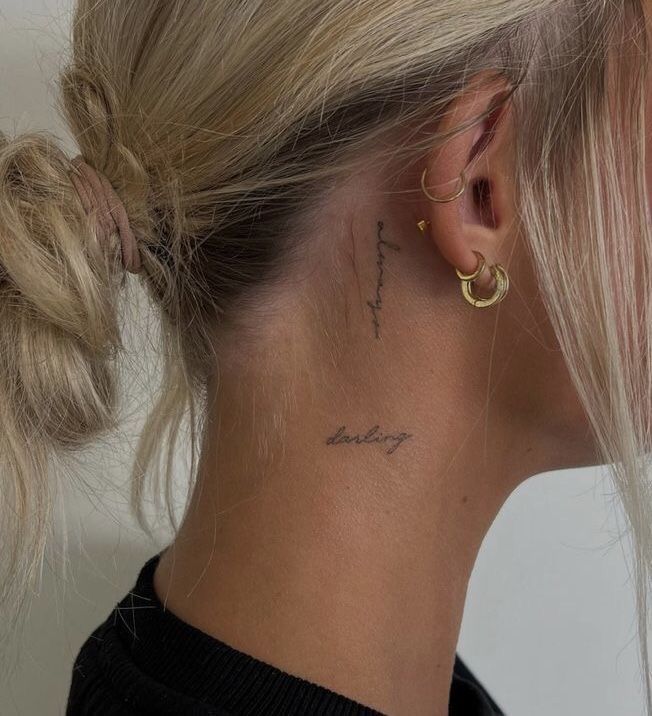 Close-up of neck tattoos with script words always and darling on a woman with blonde hair and gold earrings.