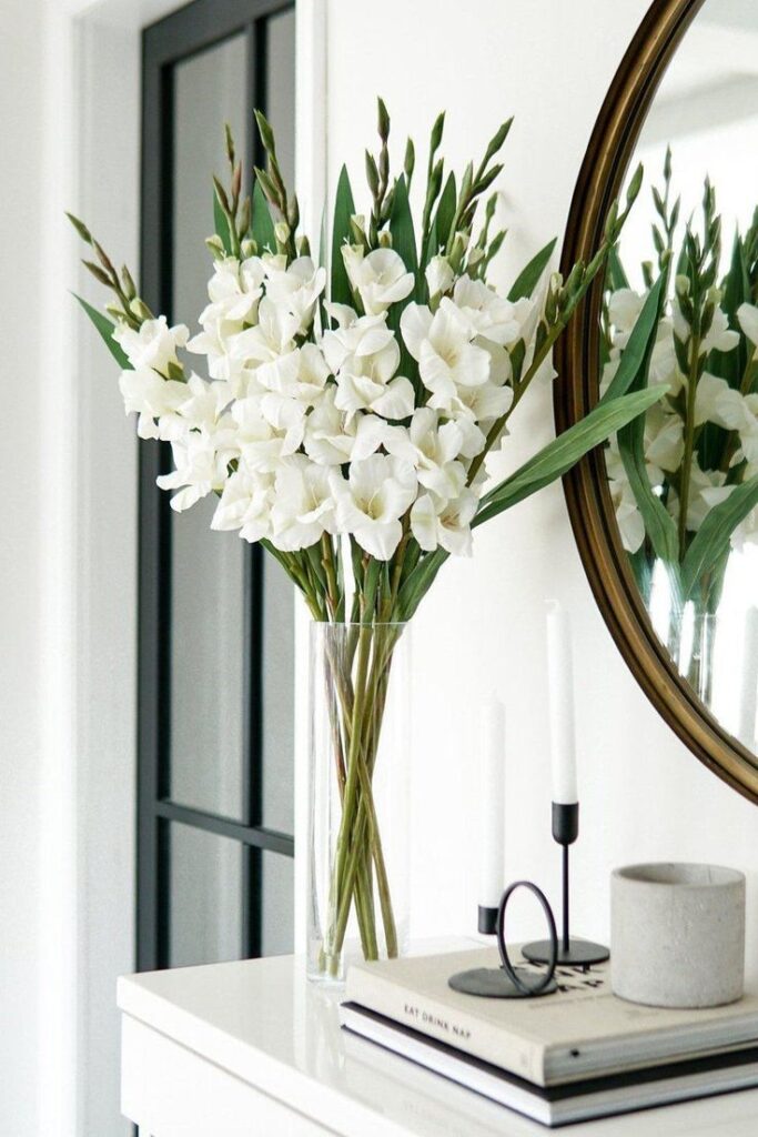 White gladiolus flowers in a glass vase on a modern white table, complementing minimalist decor in a bright room.