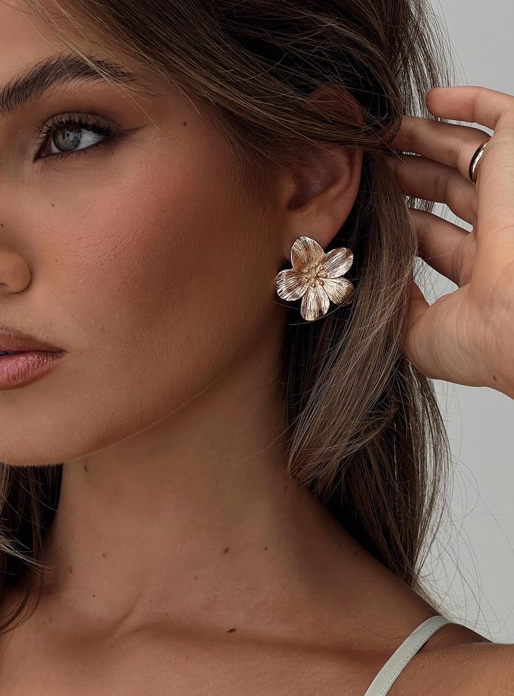 Woman wearing a large floral earring, showcasing elegant fashion jewelry style.