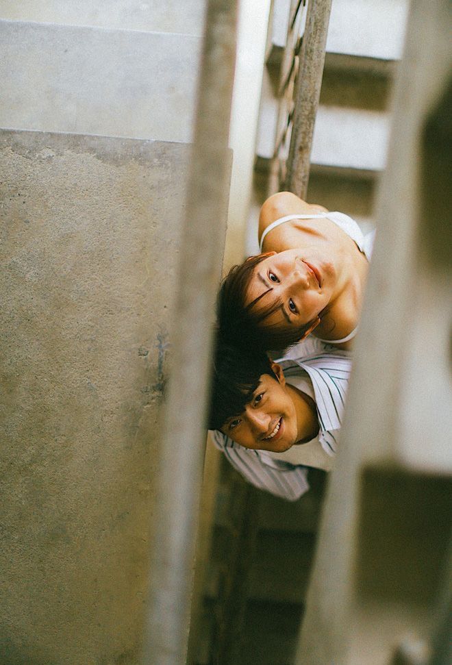 Two people smiling and looking up through staircase rails, captured from above.