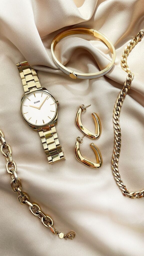Elegant gold jewelry set on silk fabric, featuring a watch, bracelet, necklace, and earrings for a luxurious look.