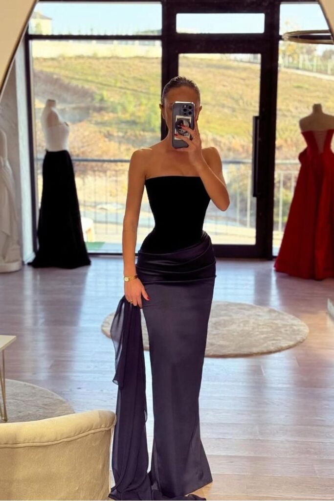 Woman in elegant black evening gown takes mirror selfie in stylish showroom.