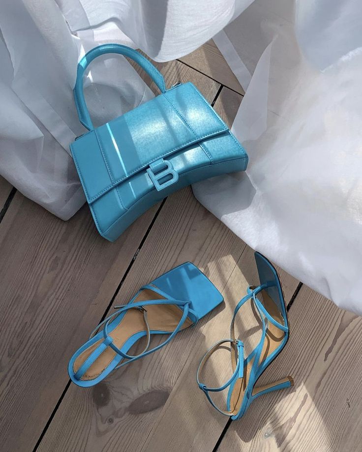 Elegant blue handbag and heels on wooden floor with soft light and white drapes. Perfect for fashion inspiration.