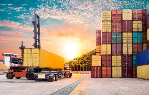 Container yard at sunset with stacked cargo containers and truck for shipping logistics.