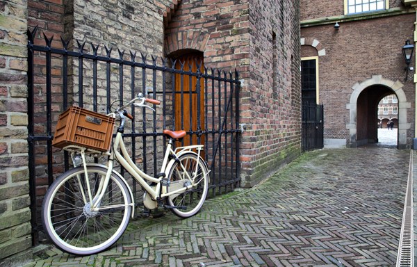 Vintage bicycle with a rear basket parked by a brick wall in a historic European courtyard.