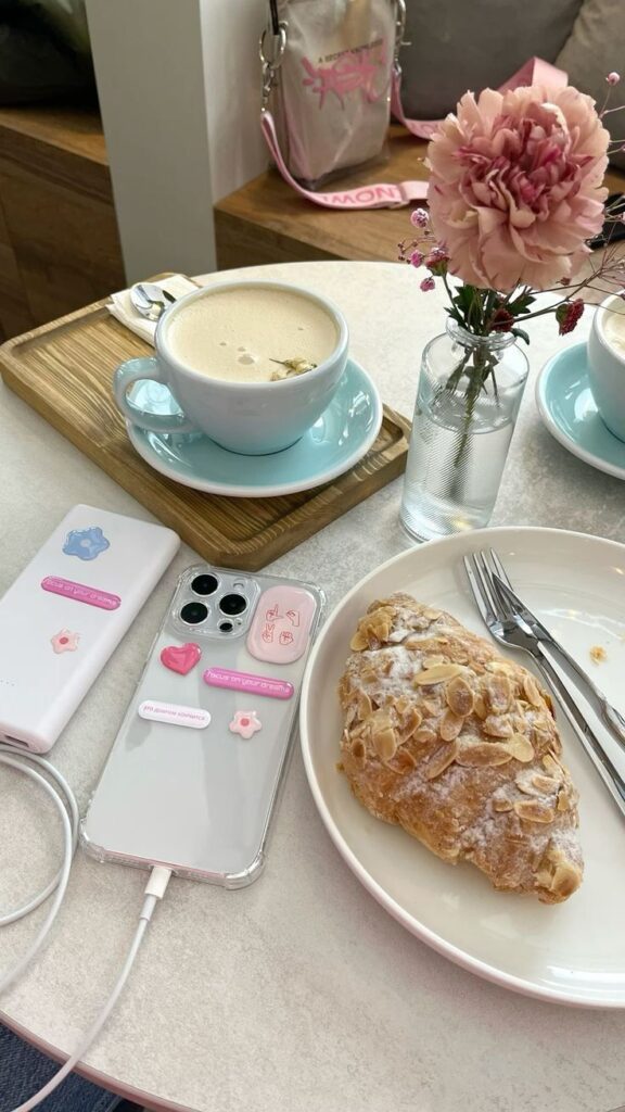 Coffee, pastry, and smartphone with motivational stickers in a cozy cafe setting with flowers.