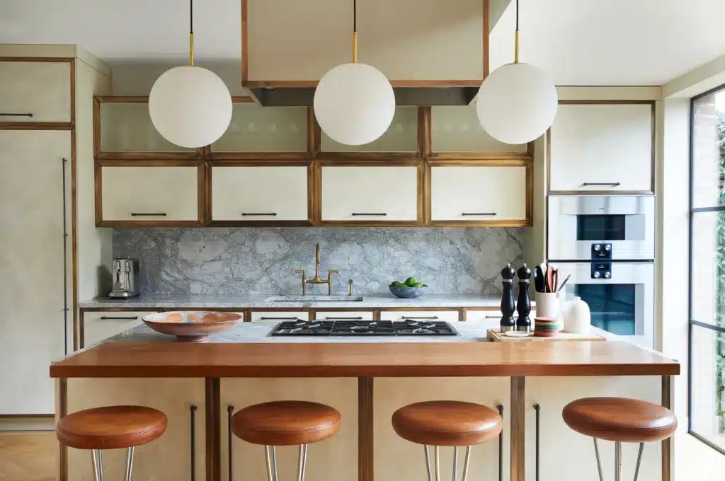 Modern kitchen with marble backsplash, pendant lights, and wooden bar stools around a central island.
