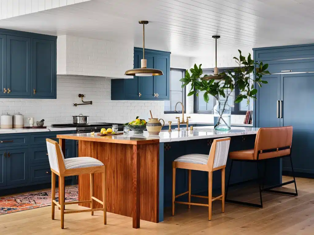 Stylish kitchen with blue cabinets, white brick walls, wood island, modern stools, and green plant centerpiece.
