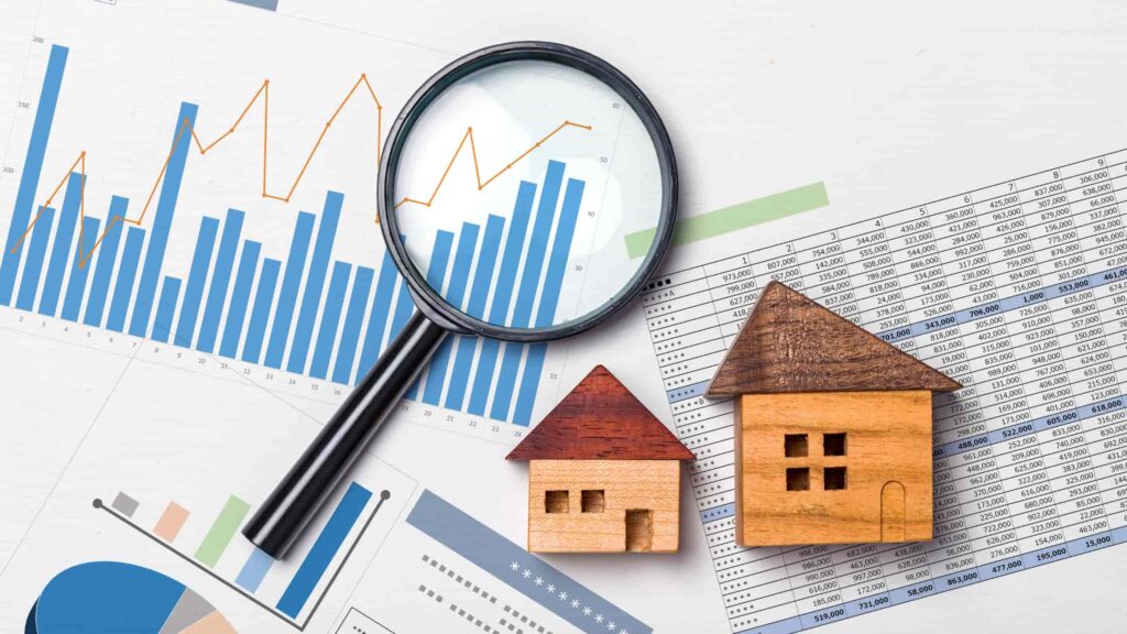 Magnifying glass over graphs and charts with wooden house models, representing real estate market analysis.
