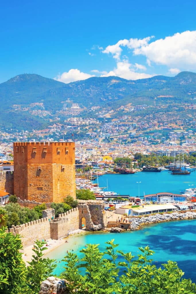 Antalya 1 Historic fortress overlooking a vibrant coastal city with mountains and turquoise sea under a blue sky. | Sky Rye Design Historic fortress overlooking a vibrant coastal city with mountains and turquoise sea under a blue sky.