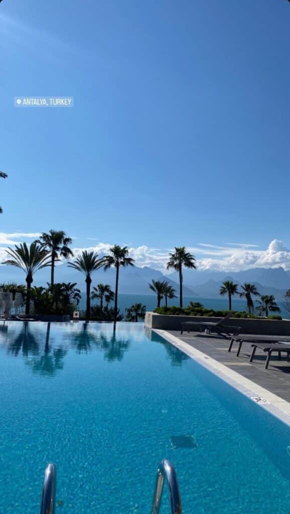 Infinity pool with palm trees and sea view in Antalya, Turkey, under clear blue skies. Perfect vacation spot.