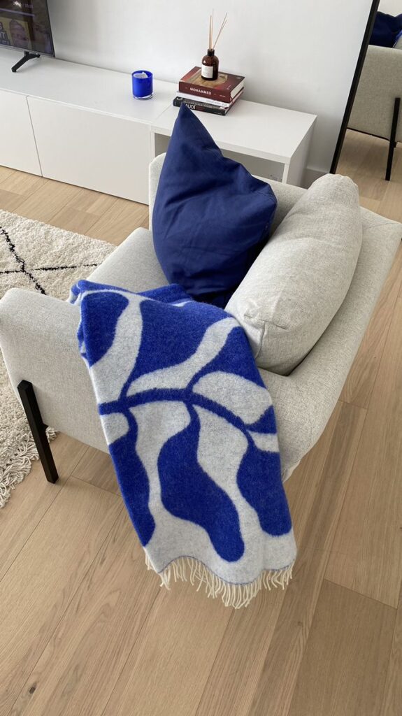 Gray chair with abstract blue blanket and cushion in modern living room setting.