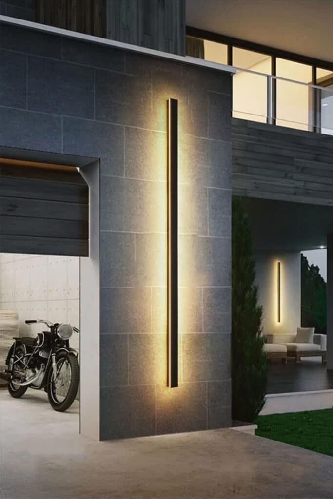 Modern outdoor wall light illuminating a contemporary home entrance at dusk with motorcycle in the garage.