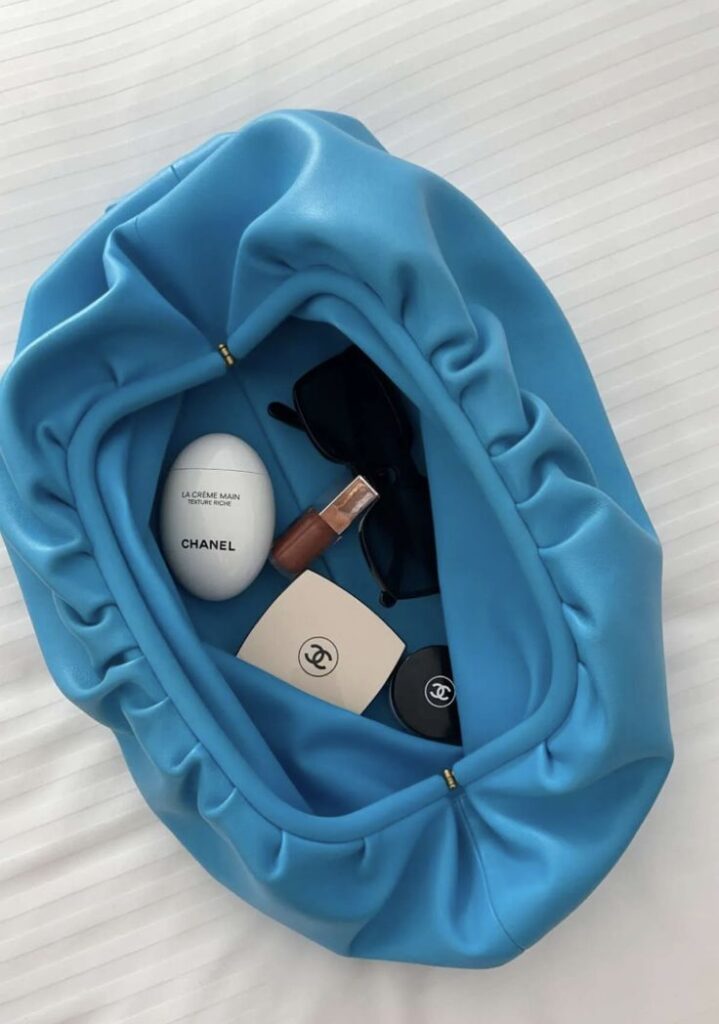 Blue bag with sunglasses, Chanel hand cream, and cosmetics on a white background.