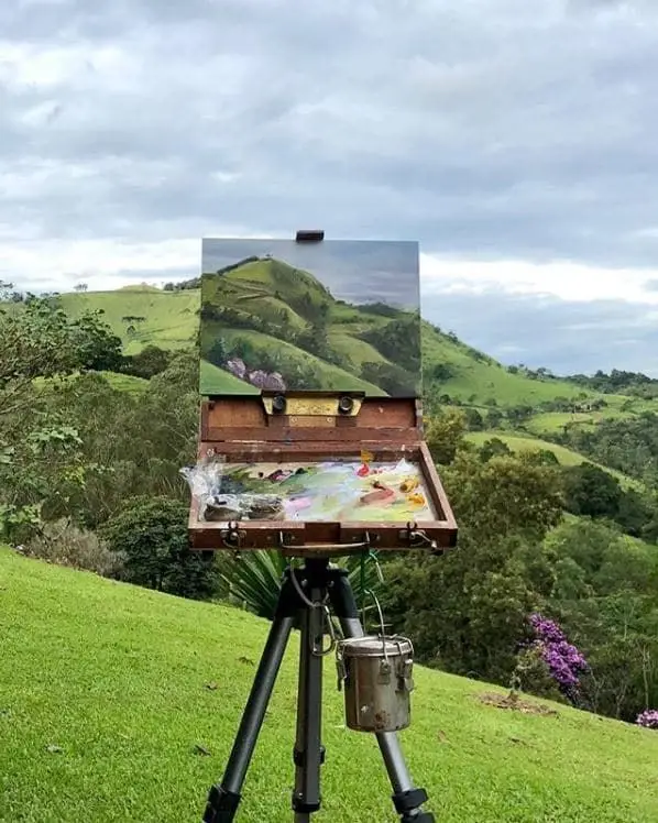 Plein air painting setup in lush green landscape, capturing scenic rolling hills and vibrant nature on canvas.
