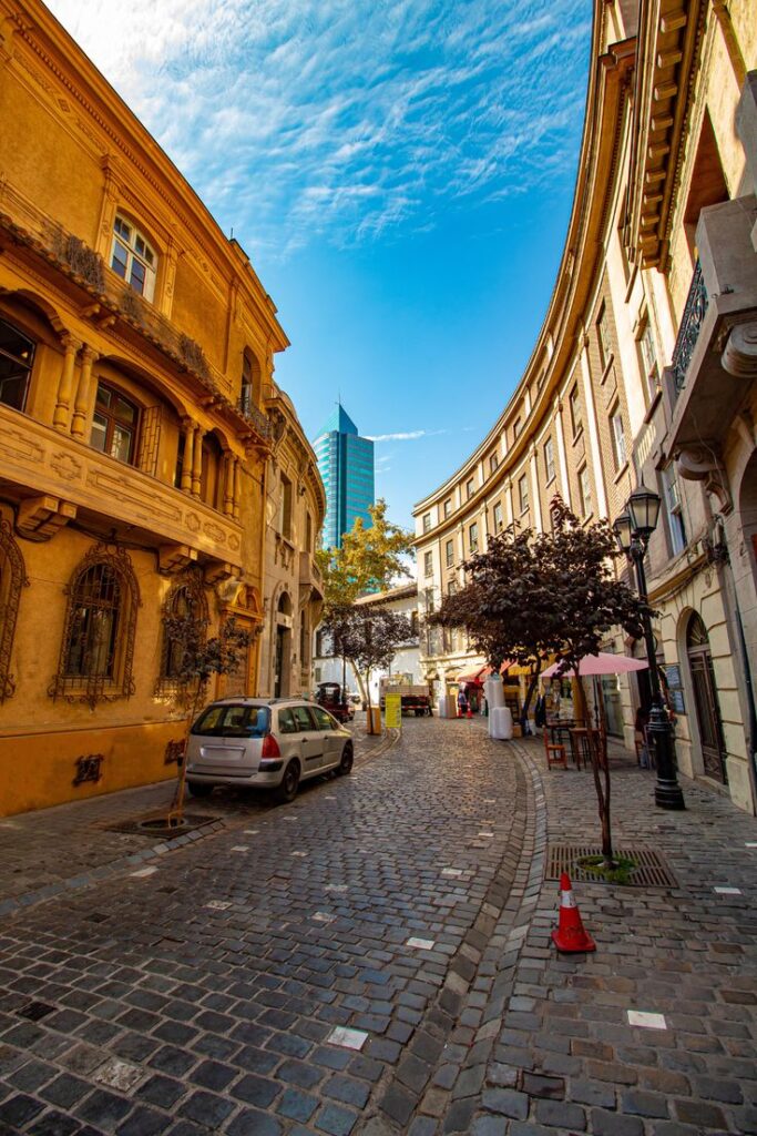 Old town cobblestone street with colorful architecture and modern skyscraper in sunny urban setting.