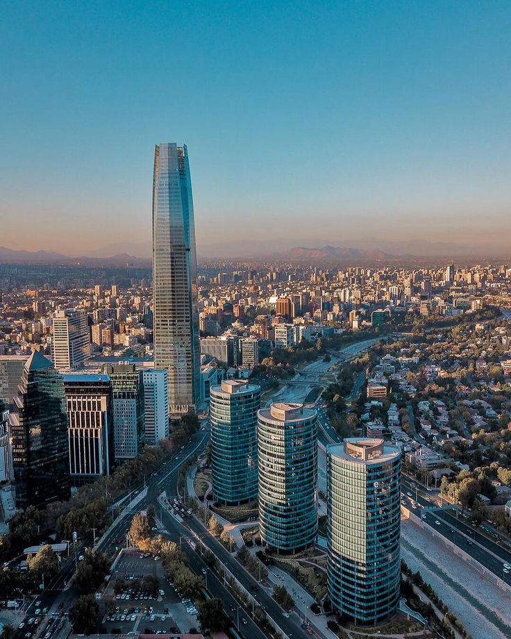 Aerial view of Santiago skyline with modern skyscrapers and mountains in the background during sunset.