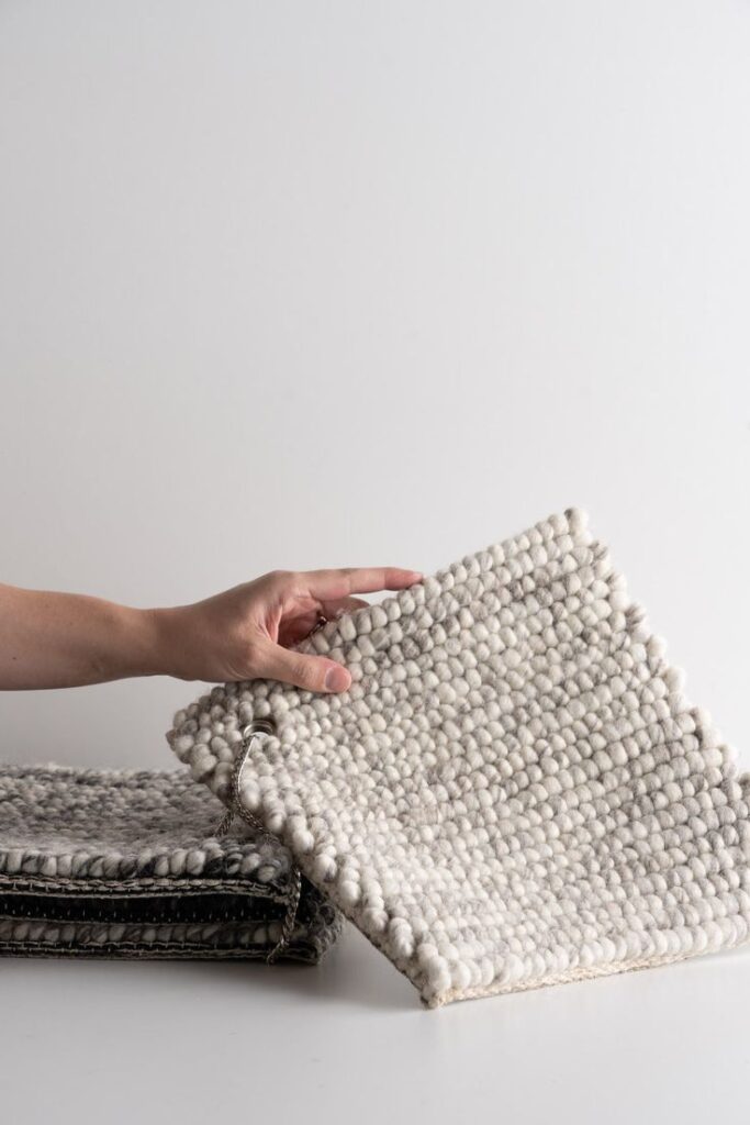 Hand holding a textured white wool sample against a stack of fabric swatches on a neutral background.