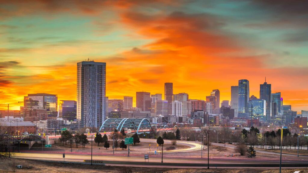 Denver skyline with vibrant sunset colors, highlighting city architecture and a foreground highway.
