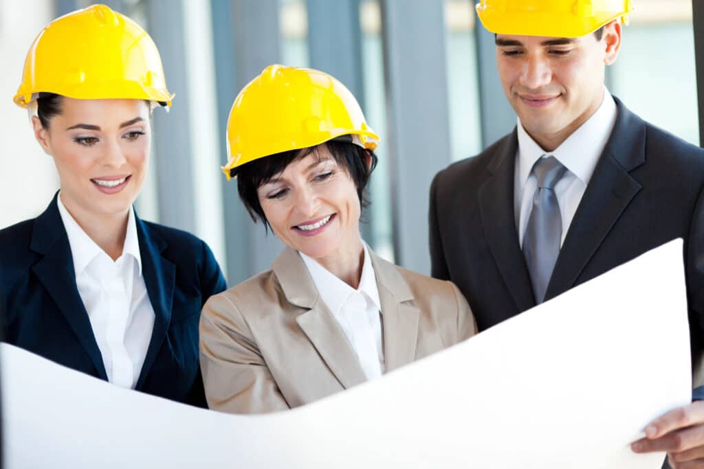 Team of engineers in yellow helmets reviewing architectural plans.