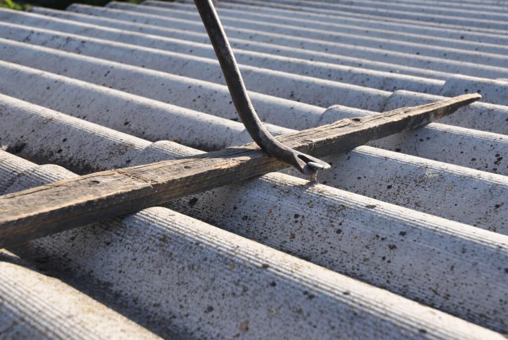 Old metal crowbar removing nails from weathered wood on a corrugated roof under sunlight.